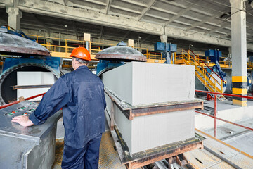 Worker in helmet loads raw blocks into open autoclaves