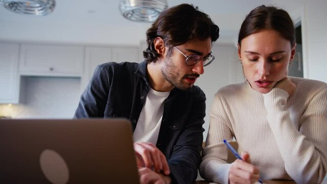 Worried young couple at home looking at laptop in kitchen counter worried about bills and cost of living crisis working out budget- shot in slow motion