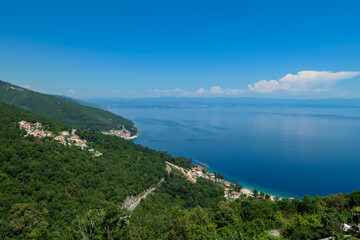 A panoramic view from above of the shore along Moscenicka Draga, Croatia. A few small towns located on the shore of the Mediterranean Sea. Lush green hills along the hills. Sunny day.