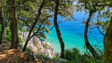 A view on the seashore from a cliff above the beach in Croatia. The sea has turquoise color and is very clean. There are a few trees growing on the steep cliffs. Stony beach. Sunny and warm day.