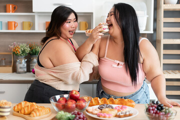 Happy Asia plus size woman eating bread with friend in kitchen at home	