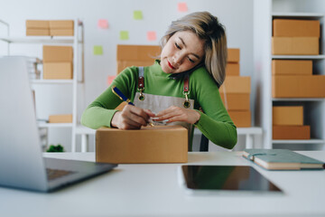Starting small business entrepreneur of independent Asian female online seller talking on the phone with a customer and packing products for delivery to the customer. and SME delivery concept