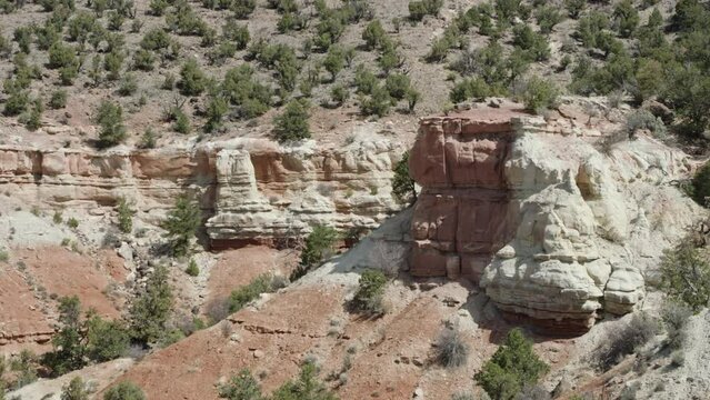 Telephoto pan across red rock cliff side with shrubs and recent rockslide 