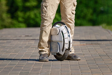 Man on electric monowheel (EUC). Stylish boy in sneakers stand alone with mono wheel. Man on electric unicycle commuting to work. Portable individual electric vehicle. . © Tricky Shark
