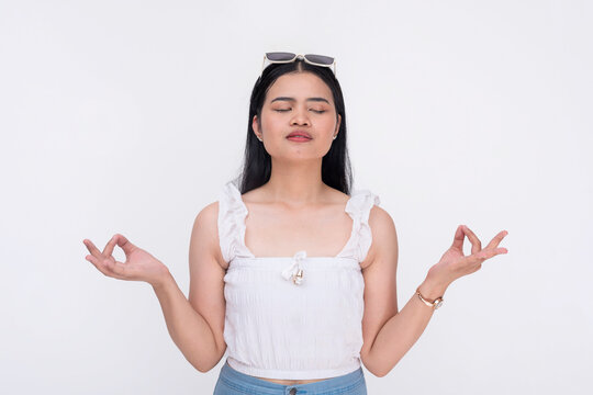 A young asian woman trying to keep calm and avoid stress by meditating and closing her eyes. A novice yoga practitioner. Isolated on a white background.