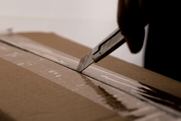 Close-up of woman's hand opening box using cutter. Hands unpacking cardboard boxes in the house.