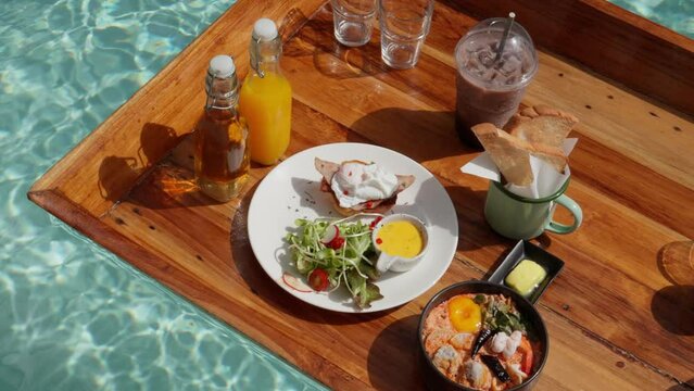 A hot, sun-drenched day sets the stage for a floating breakfast experience. Colorful treats rest atop the water's surface, inviting a refreshing indulgence amidst the warmth of a radiant summer day.