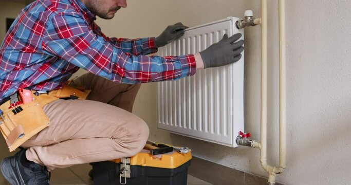 Male plumber with equipment inspects broken central heating radiator in light accommodation. Repair of device to maintain warm temperature in building