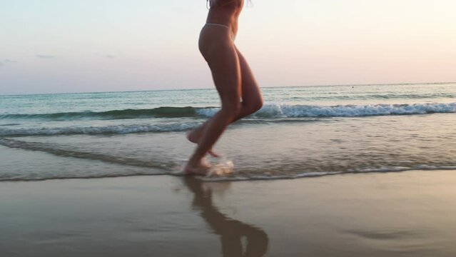 Close-up of woman's legs running on the sandy beach at sunset. girl on the beach. running along the sea at sunset.