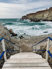 Wooden staircase leads to a descent to the beach. Rocky shore and stormy sea