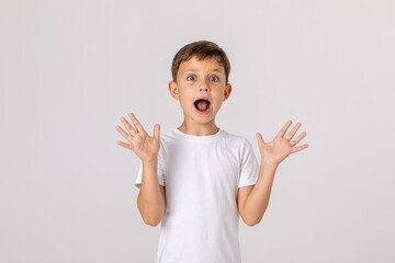 Portrait of scared little boy wearing white t-shirt making a grimace with his mouth open and hands...