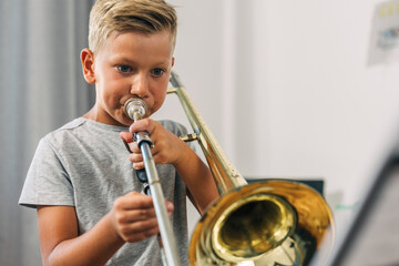 Young boy practicing trombone alone. - obrazy, fototapety, plakaty