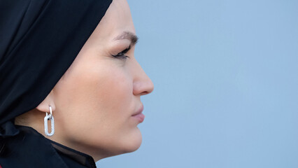 Muslim woman face in profile standing with serious and upset expression at wall of building. Woman in black headscarf worried about country future