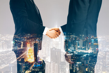 Businesspeople shaking hands on blurry night city background. Teamwork, success and partnership concept. Double exposure.