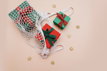 Red, green gift boxes lie in an eco-friendly white string bag on a beige background with gold stars. top view. Copy space