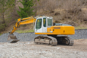 A crawler excavator with a rotating house platform and continuous caterpillar track, and a scoop bucket. On a site near Forni Avoltri in Carnia, Udine, Friuli-Venezia Giulia, N.E. Italy