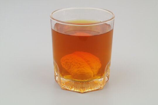 Brain drowned in glass of alcohol on gray background. 