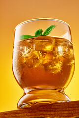 Close up glass of refreshing iced tea with ice cubes and mint leaves. Studio shot from a low angle. Vertical frame.