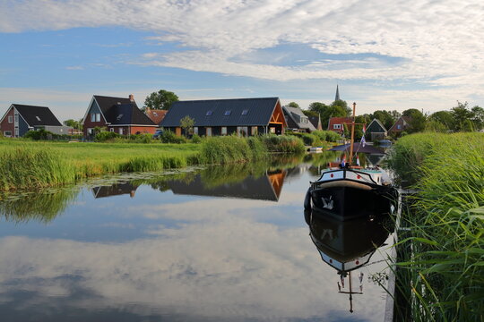 Reflection of houses and a mooring boat  along a canal in Baard, Friesland, Netherlands, a small village located 13km West from Leeuwarden