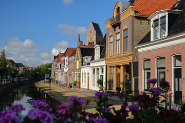 Fototapeta na wymiar Colorful house facades along Kleine Dijlakker street in Bolsward, Friesland, Netherlands, with the bell tower of Martinikerk (St Martin church) in the background