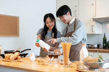 Happy Asian couple making pancakes, mixing pancake flour in a lovely minimal kitchen together.