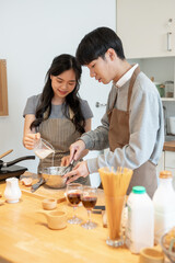 A lovely Asian couple is having a cooking date at home and enjoys making pancakes in the kitchen