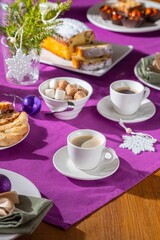 Obraz na płótnie Canvas Coffee table setting with white tableware in Christmas style on a table with a purple tablecloth. Merry Christmas concept. Receiving guests,