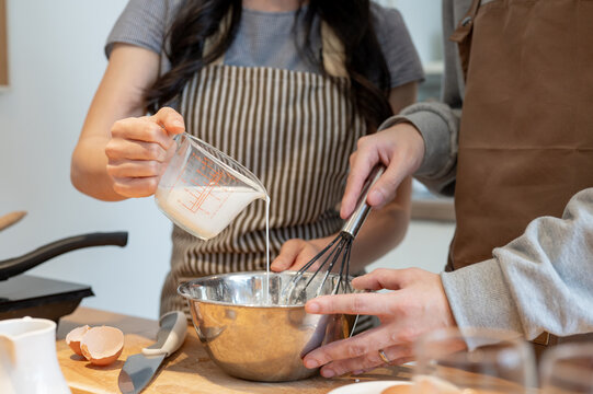 Close-up image of a couple making pancakes in a lovely minimalist kitchen together.