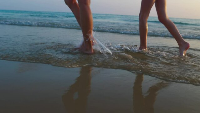 Close-up Of Legs, Mother And Child Are Walking Along The Sandy Beach At Sunset. Walk Along The Sea At Sunset. Family Holiday.