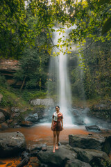 A young beautiful Asian girl explores a waterfall during her summer vacation in Laos, Asia