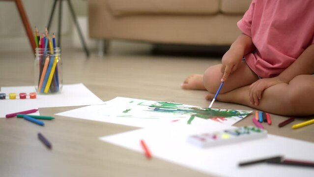 Little cute girl creating and water color painting activity with paint brushes in living room at home. Kids activity. Child physical, Emotional, Cognitive development concept.