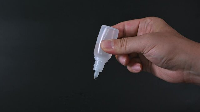Man's hand using eye drops on black background