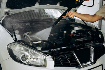 Washing the car engine under strong water pressure. Car maintenance, care and cleanliness. Worker...