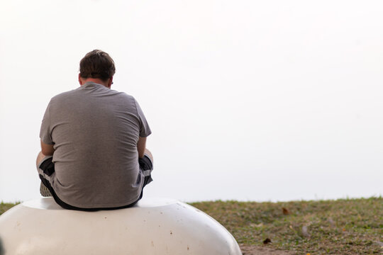 A depressed young man sat by the reservoir alone with a depressed feeling. The young man sat by the reservoir, depressed and staring into the water with emotional strain. Copy Space for text.