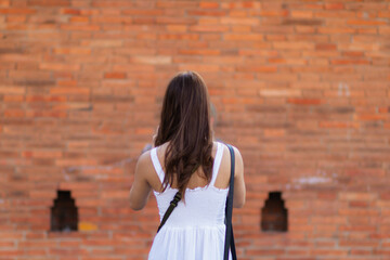 Asian tourists traveling and taking in sights of ancient city wall in Chiang Mai, Thailand, alone in summer. Back view of young female tourist taking walk taking in view of city wall and copy space