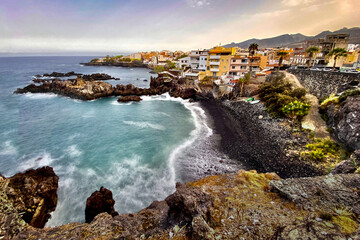 Fototapeta premium Exclusive beach of Tenerife. Beautiful sunset by the Atlantic Ocean. Epic volcanic rocks, cliffs, black sand, waves, turquoise water. Premium landscape from pure nature, town Alcalá, Canary Islands 