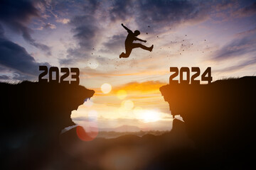 Man jumping from 2023cliff to 2024 cliff with cloud sky and sunlight.