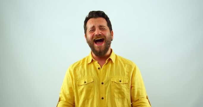 A middle-aged man is  in a studio, looking at the camera and laughing. His mouth is wide open, and he appears to be having a hilarious laughing fit