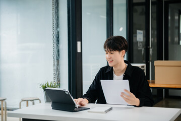 Obraz premium Confident Asian man with a smile standing holding notepad and tablet at the office.