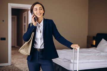 Business woman in a hotel room talking on the phone and carrying baggage
