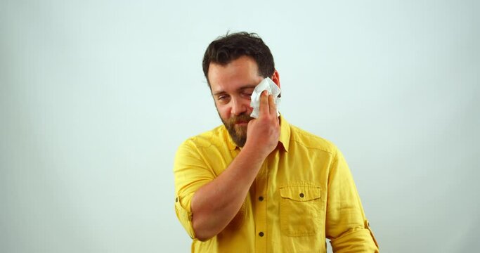 A middle-aged businessman is  in a studio, looking at the camera and wiping sweat from his brow. He appears to be feeling stressed or exhausted.