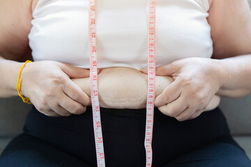 An obesity using measuring tape to show the real size. Chubby fat woman using measure tape