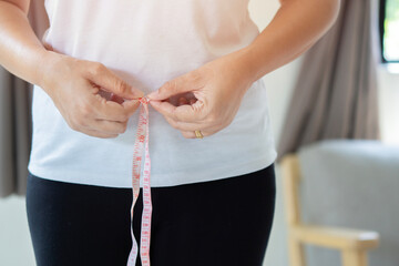 Cropped image of young fat overweight woman wearing sportswear measure the waist with measuring tape