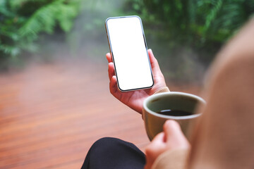 Mockup image of a woman holding mobile phone with blank white desktop screen while drinking coffee...