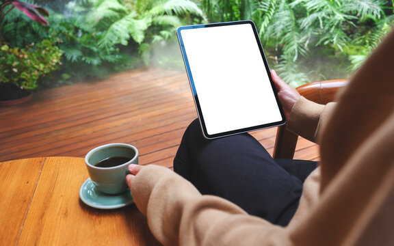 Mockup image of a woman holding digital tablet with blank white desktop screen while drinking coffee in the garden
