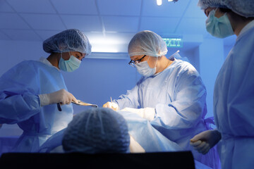 Two nurses and a surgeon all wearing scrubs and surgical gear are operating on a patient and the...