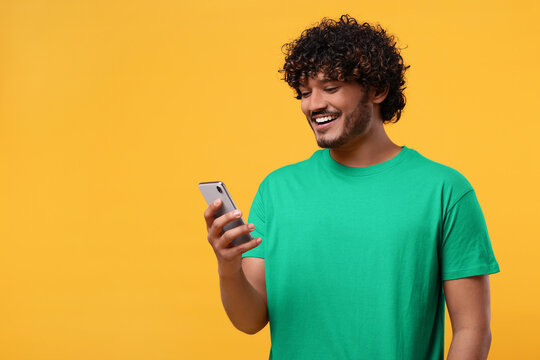 Handsome smiling man using smartphone on yellow background, space for text