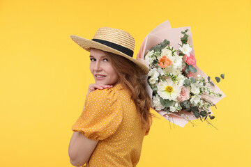 Beautiful woman in straw hat with bouquet of flowers on yellow background