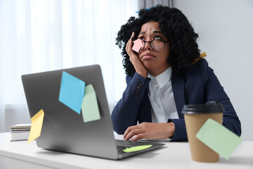 Deadline concept. Stressed woman sitting near laptop in office. Many sticky notes everywhere as...