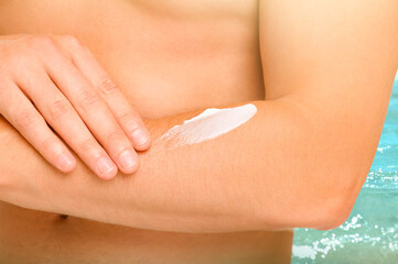 Sun protection. Man applying sunblock onto skin near sea, closeup